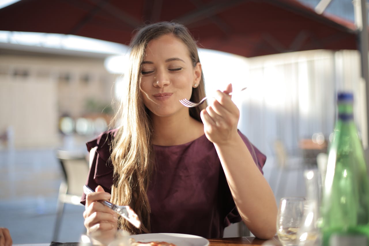 services-02 A woman savoring her meal with a smile, dining outdoors in a pleasant setting.